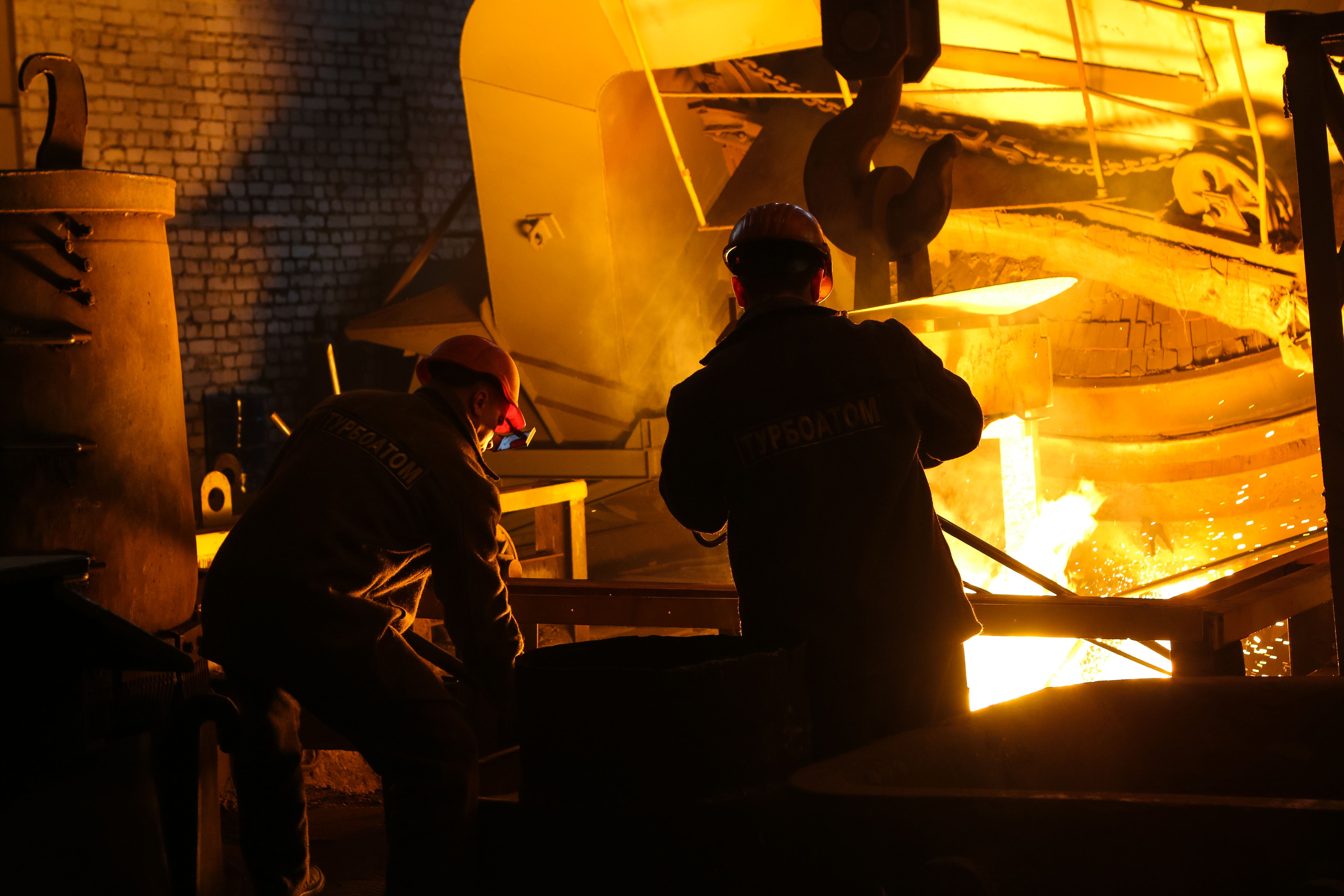 Steelworkers tending a glowing furnace in a steel mill.